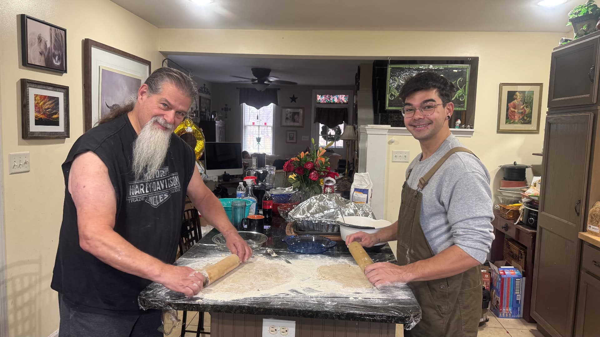 Two men rolling pie dough on a floured kitchen counter