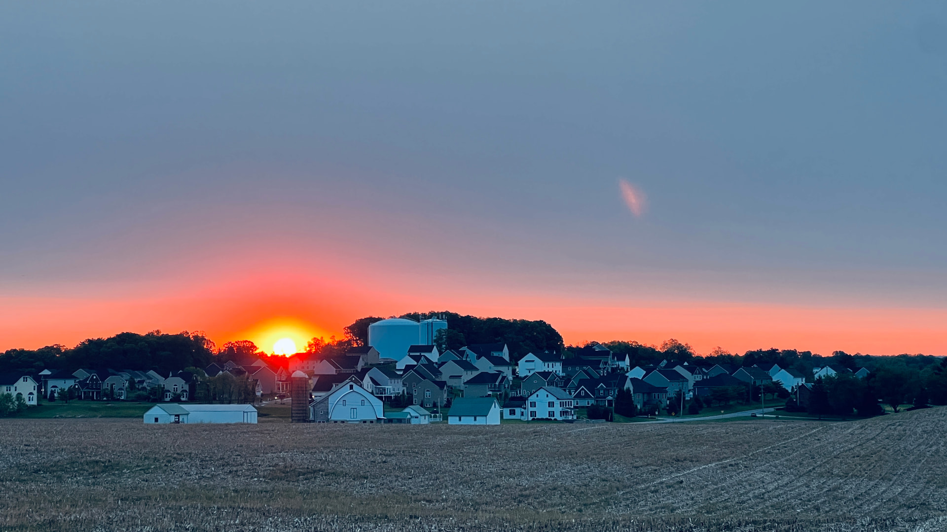 Sun setting behind a barn and silo at the edge of a stubble field