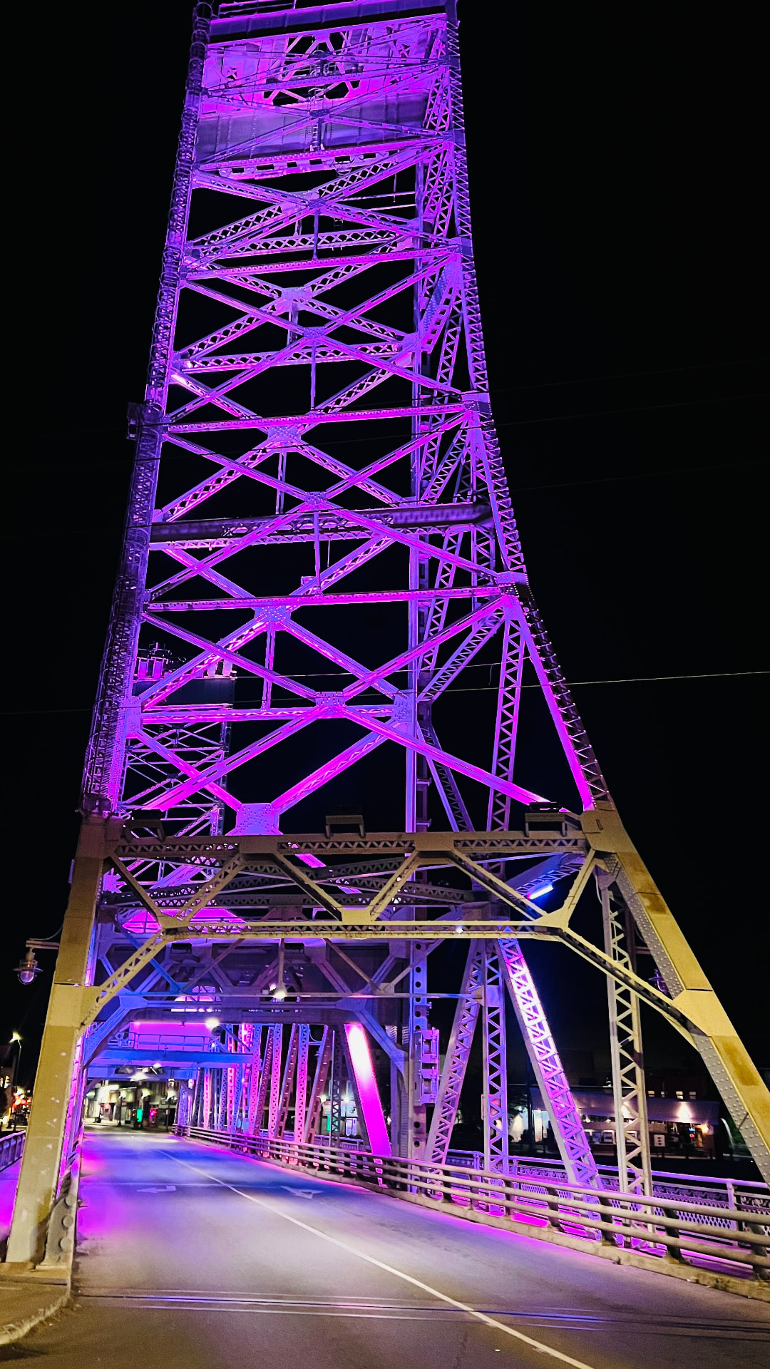 Looking up through the lit steel truss of the bridge from the roadway