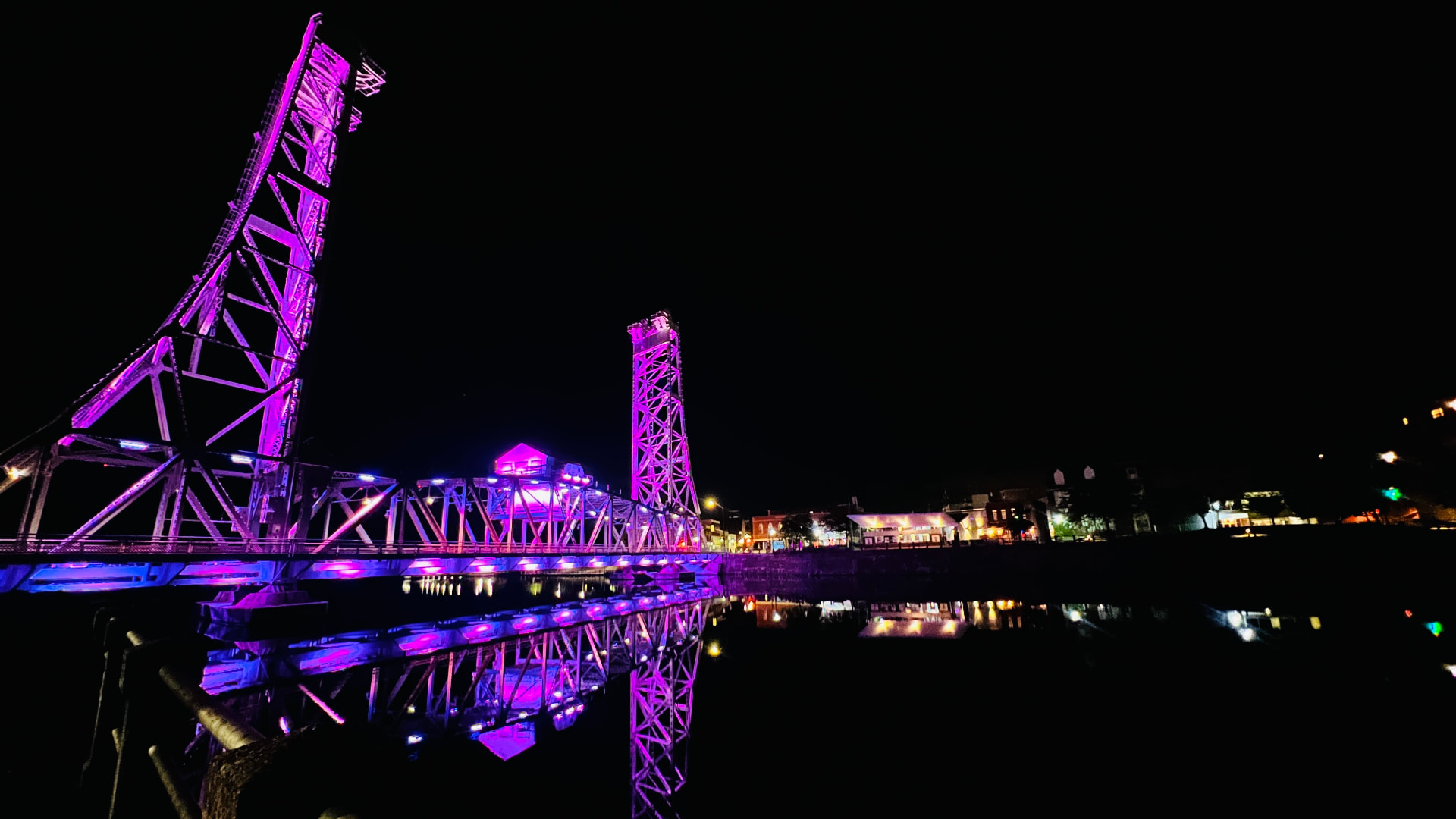 A lift bridge at night, lit violet and reflected in still water