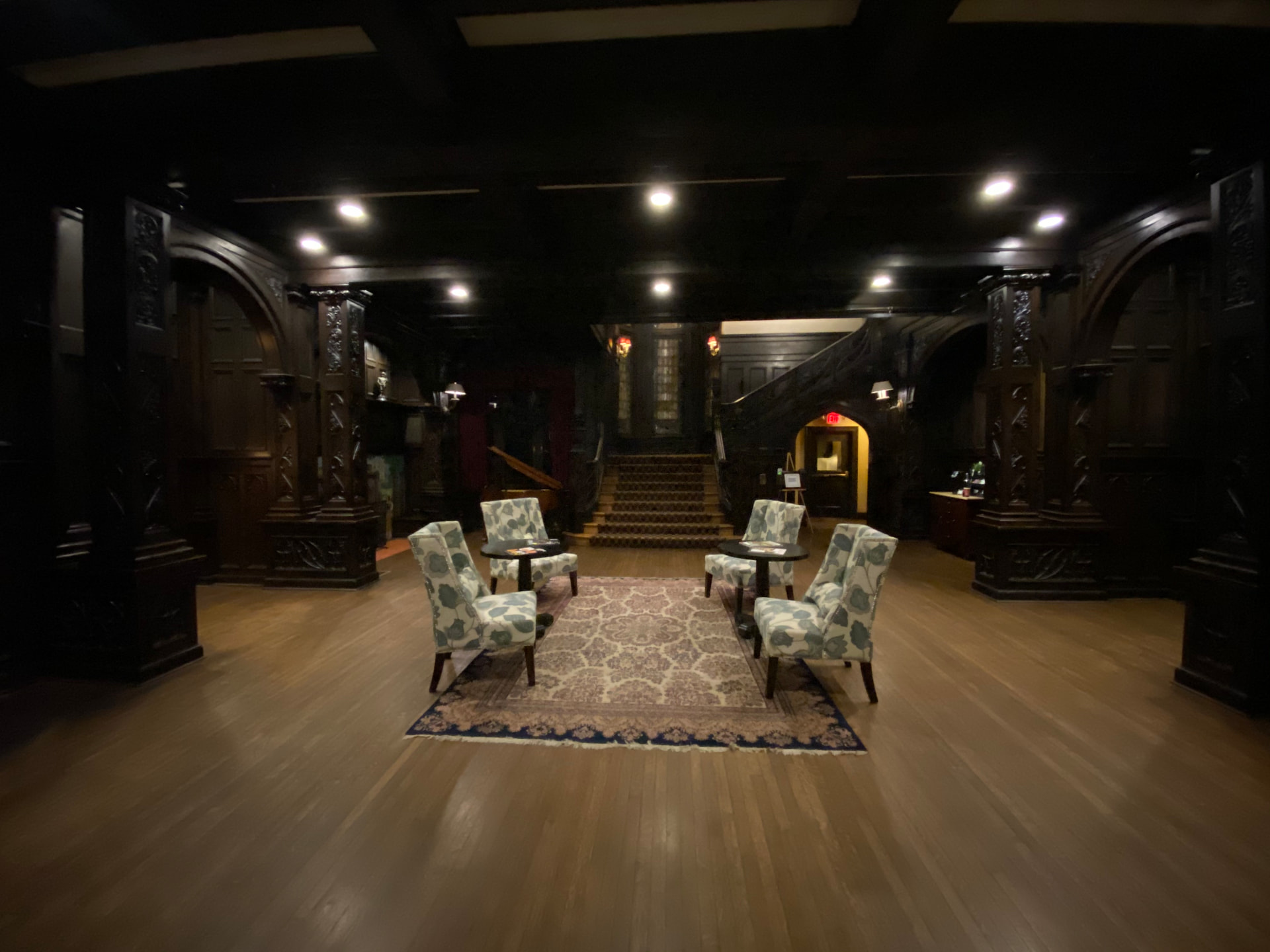 A dark panelled hall with four chairs drawn around two small tables
