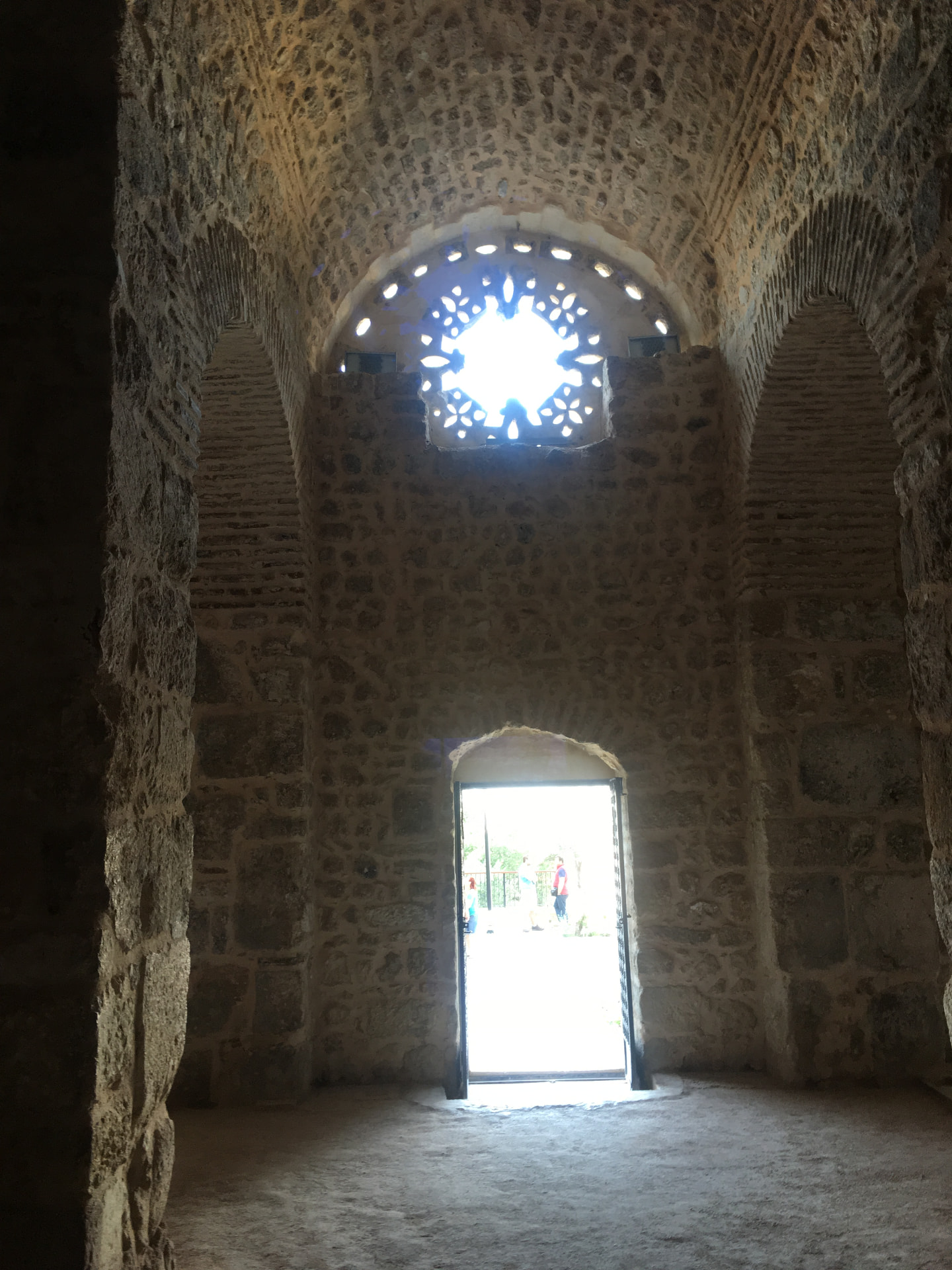 A dim stone chamber with light falling through an open doorway and a pierced rose window above