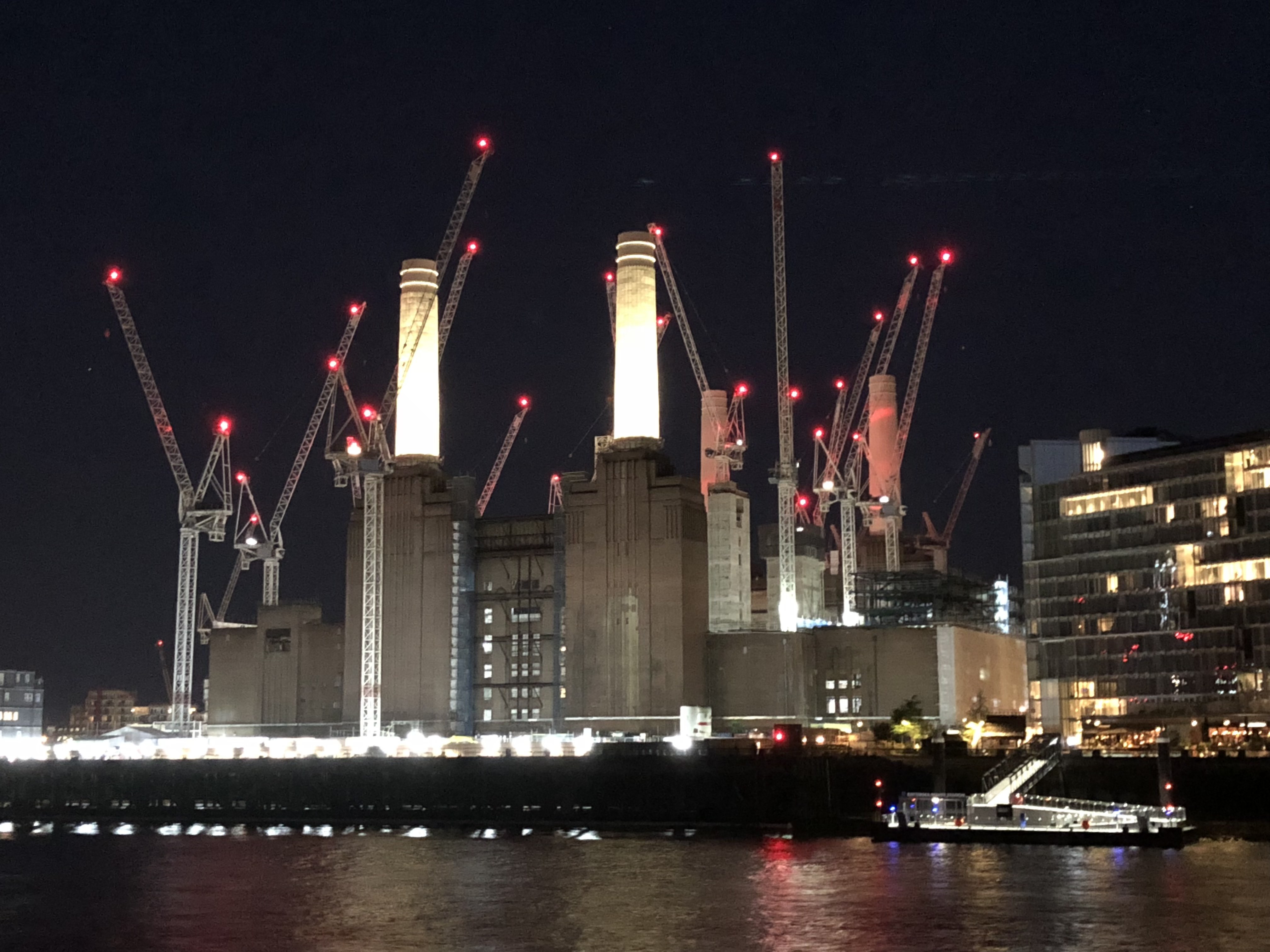 Battersea Power Station at night, floodlit chimneys ringed by construction cranes