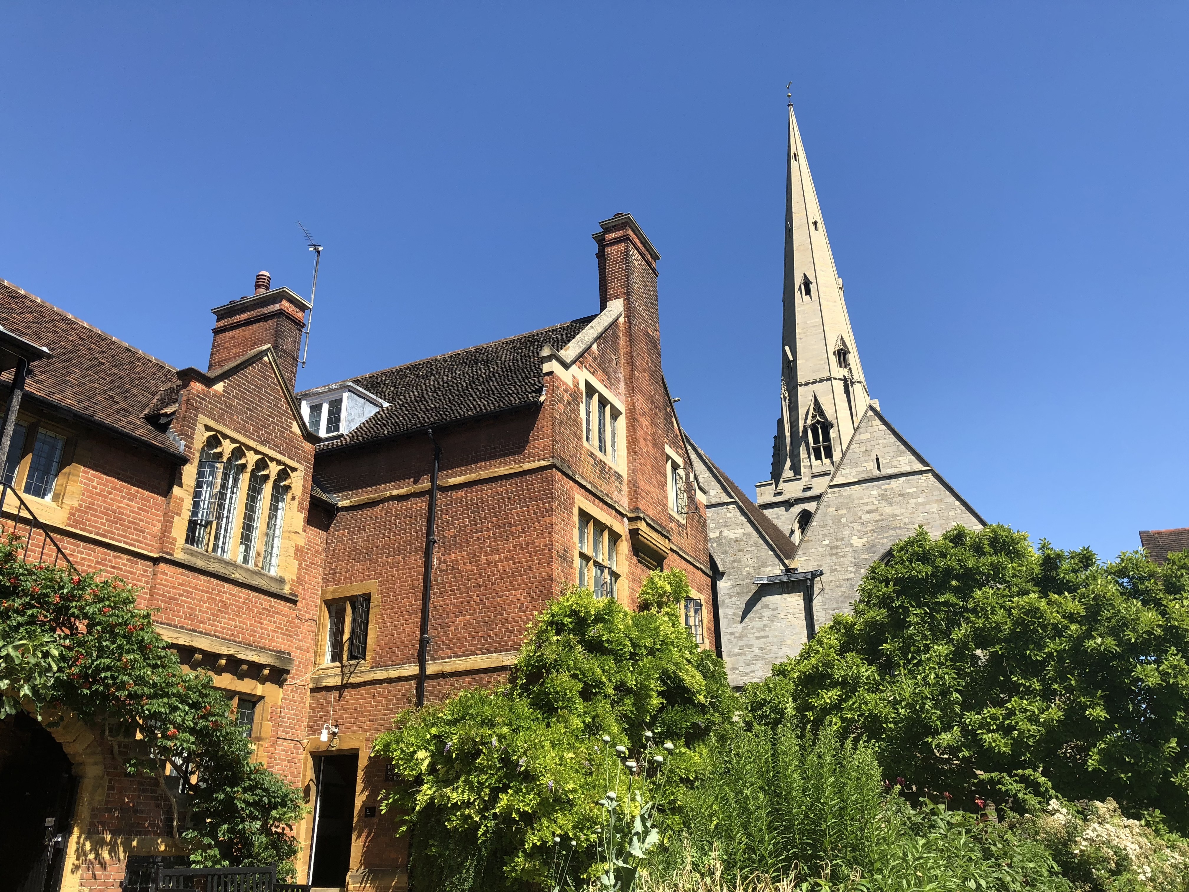 A brick college court in full sun, a stone spire rising behind the roofline