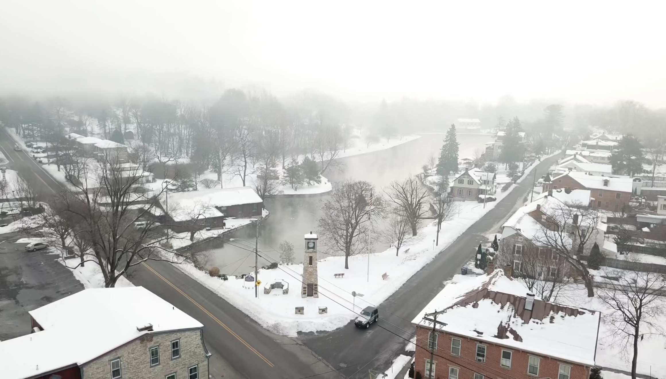 A small town under snow and fog, clock tower beside a still millpond